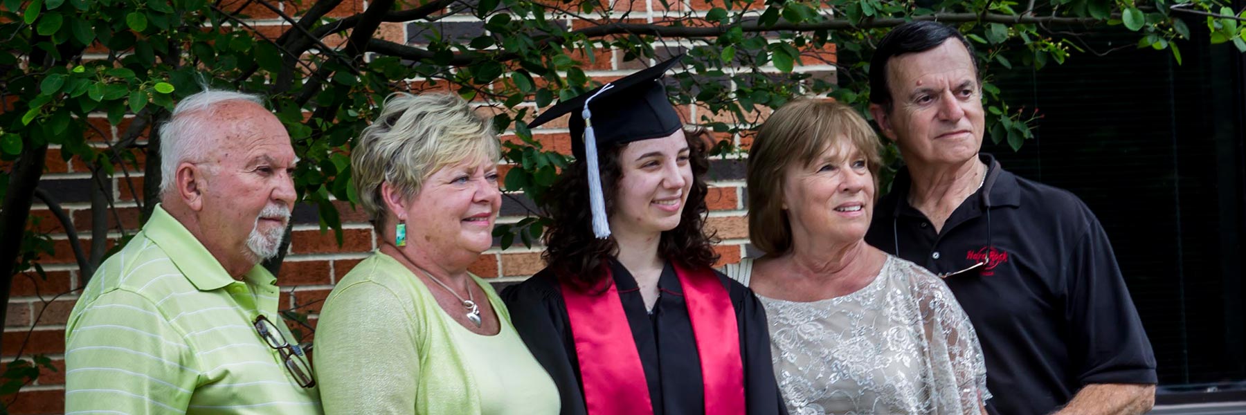 A gray-haired couple and a middle-aged man and woman take pictures with a happy graduate