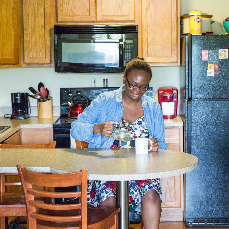 Female student pouring tea in her kitchen in the lodge